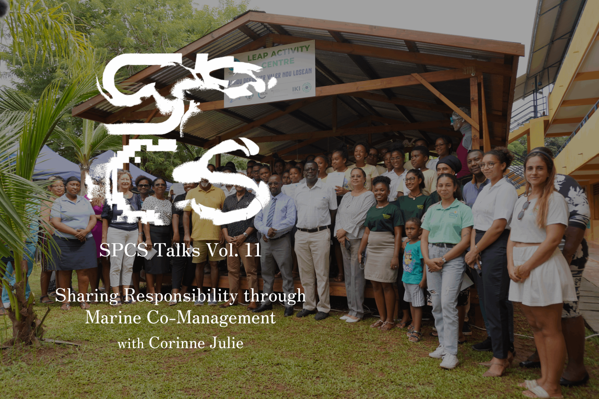 A photo of several smiling people standing in front of a wooden structure labeled