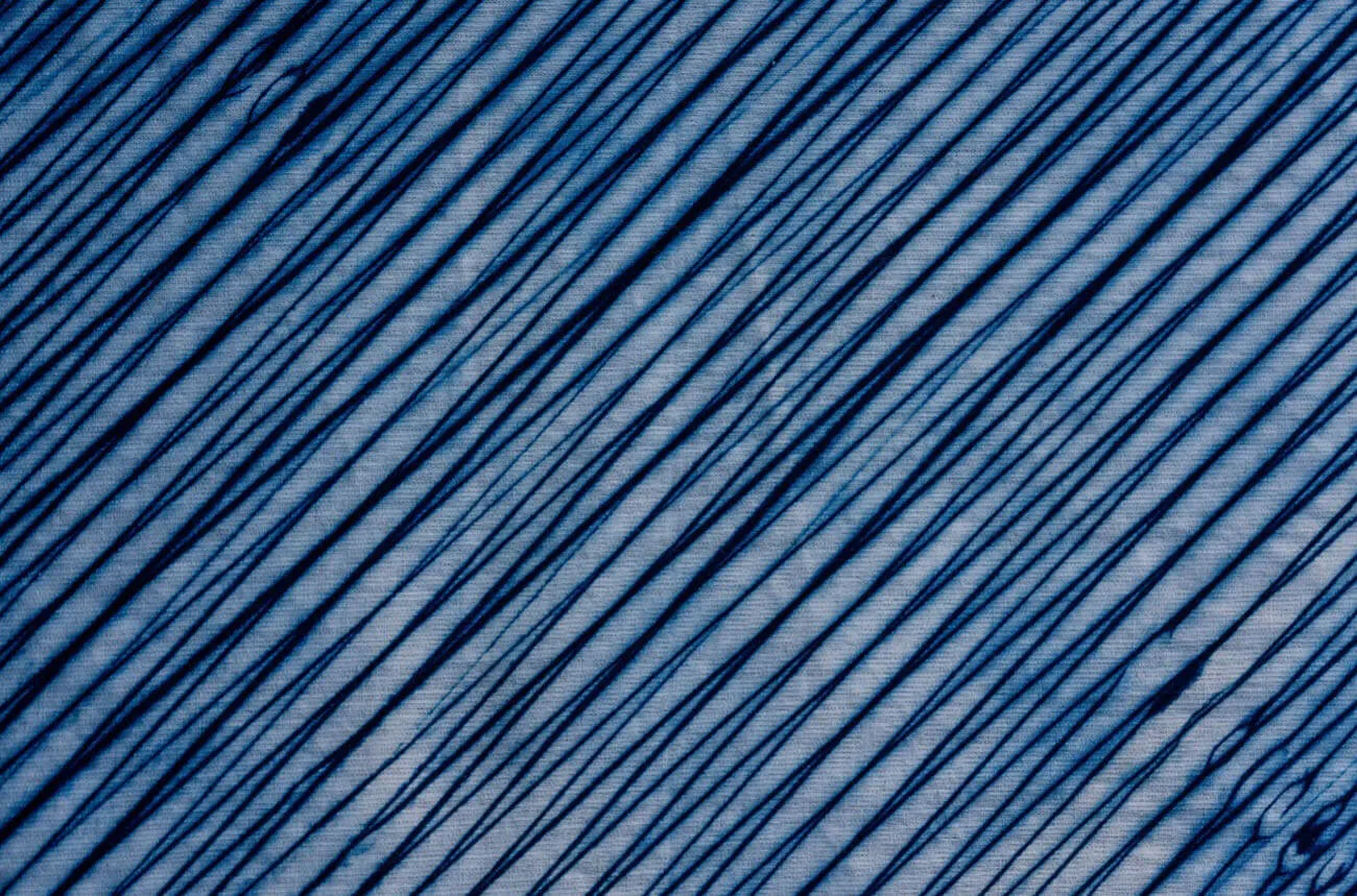 Close-up of an Arimatsu Arashi Shibori textile. Countless indigo-blue stripes run across the fabric, revealing a bold and dynamic gradient pattern.