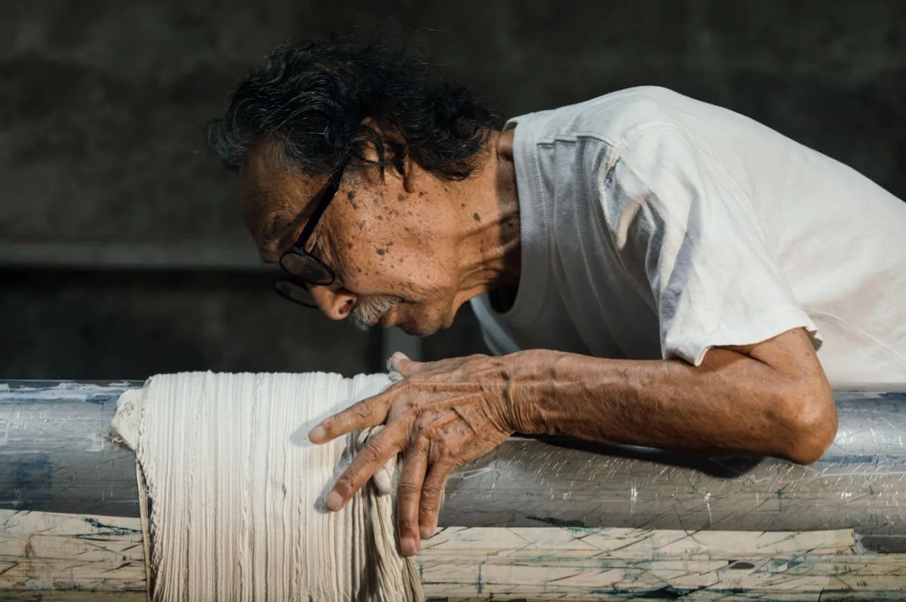 The process of Arashi Shibori: Kaei Hayakawa wraps a piece of white fabric around a rod in a spiral, using his fingertips to tightly bind the cloth, carefully embedding the pattern into it.