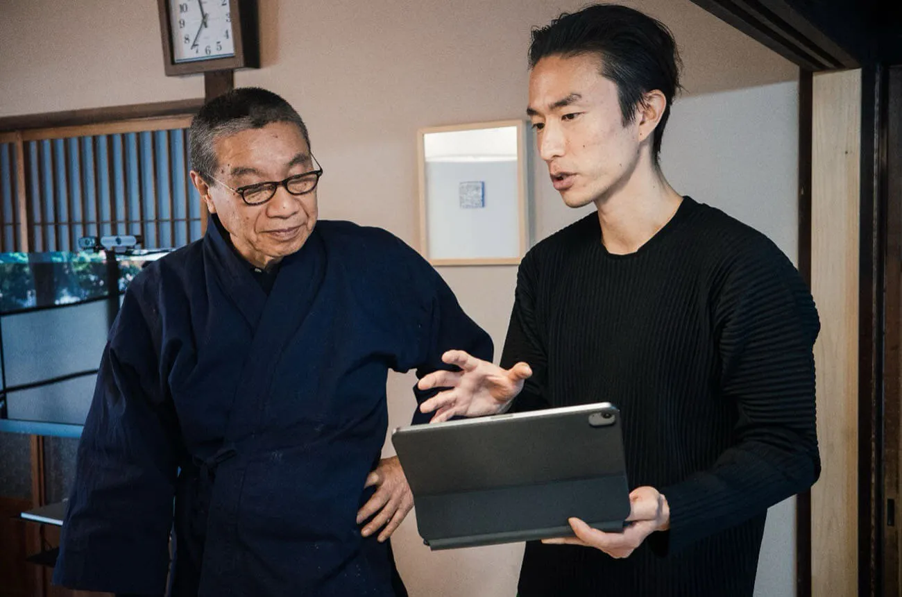 Hiroshi Murase (left), a fourth-generation artisan of Arimatsu-Narumi Shibori, discusses archiving methods with Hiroki Yoshioka (right), the project lead from DENSO, while looking over a tablet screen together.