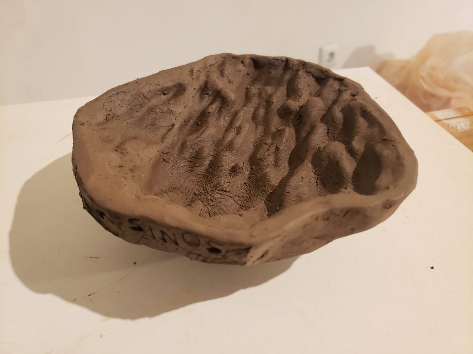 A photo of a brown clay form with sound waves engraved into it.